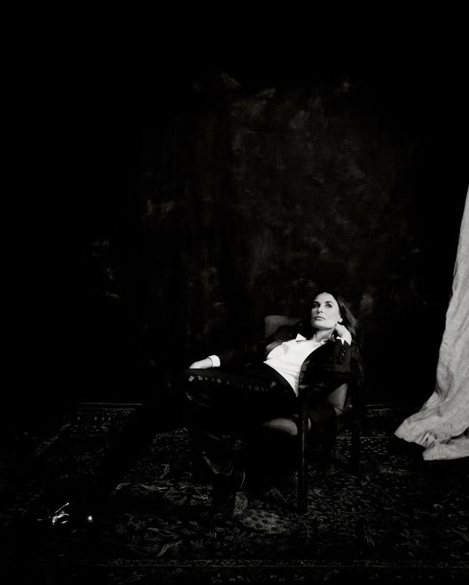 Black and white photograph of Demi Moore seated in a darkened room
